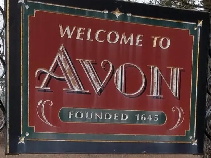 Welcome to Avon, Connecticut town sign surrounded by flowers, with trees in the background. The sign notes the town was founded in 1645.